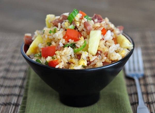 Black bowl full of Hawaiian fried rice with pineapple and tomato chunks.