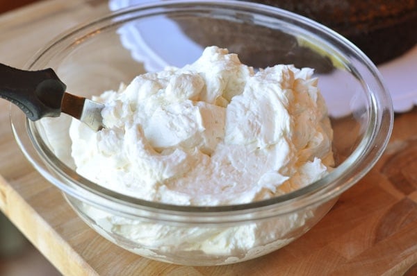 A glass bowl full of white frosting with an offset spatula inside the bowl. 