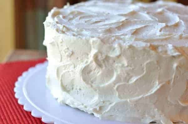 A two-layered cake cake sitting on a white cake platter, covered in white frosting. 