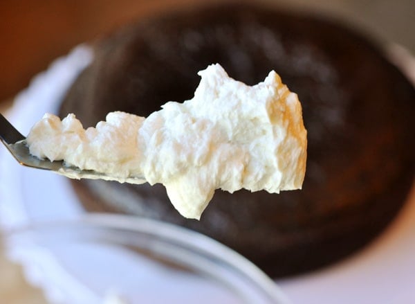 A scoop of white frosting on an offset spatula, with an unfrosted chocolate cake in the background. 