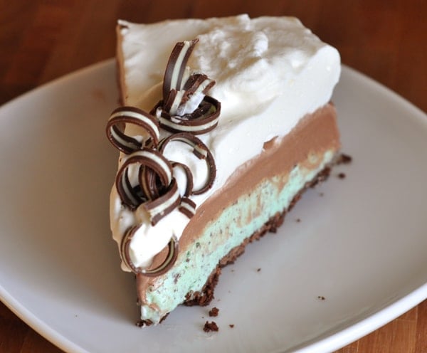 A slice of pie with a mint ice cream base, chocolate middle, and whipped cream and chocolate curls on top. 