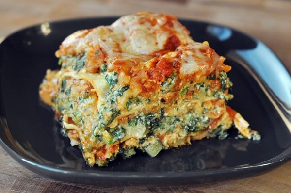 Slice of veggie lasagna on a black plate.