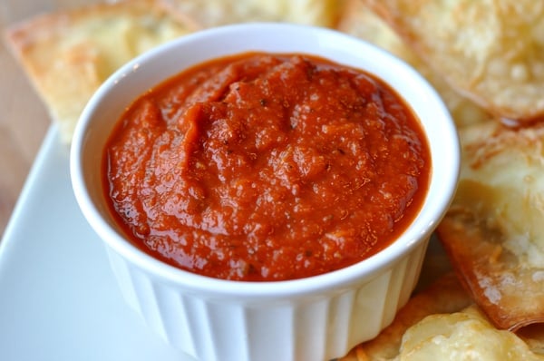 White ramekin filled with marinara sauce with garlic bread around the side, on a white platter.