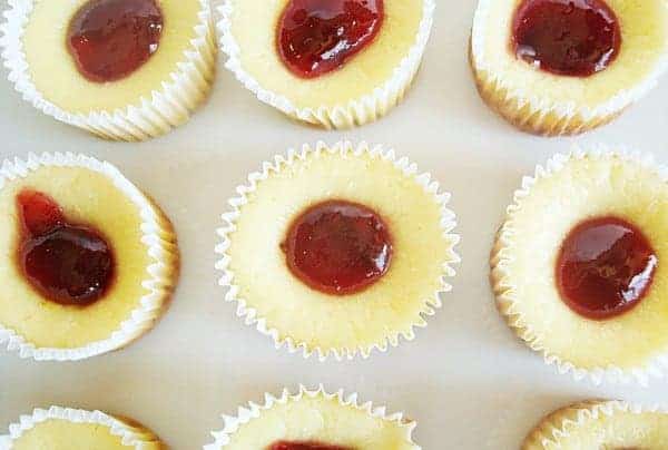 Top view of cheesecakes in white muffin liners with dollop of raspberry in each center.