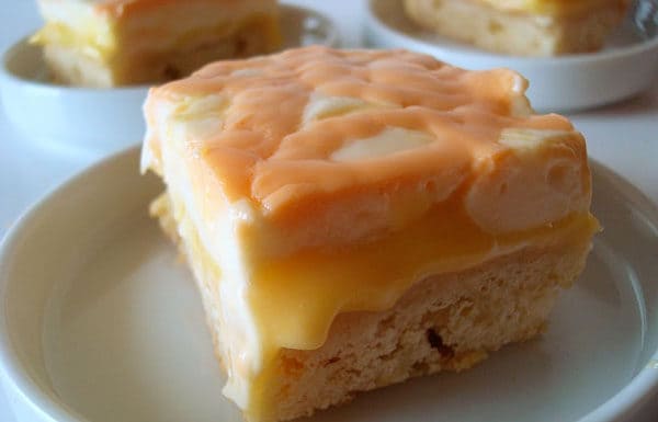 Bar with shortbread crust, orange curd middle, and cream top on a white plate.