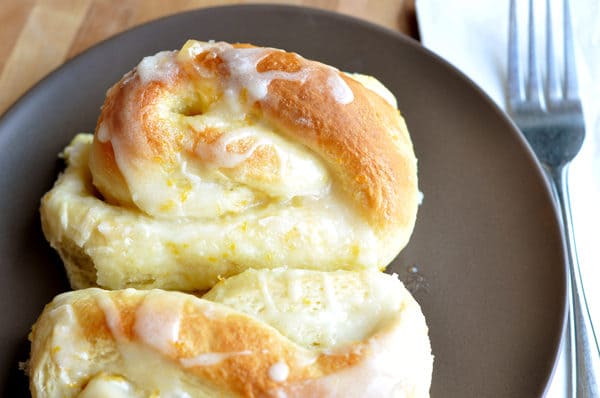 Top view of golden orange glazed sweet rolls on a brown plate.