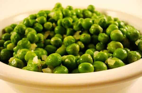 White bowl full of cooked peas.