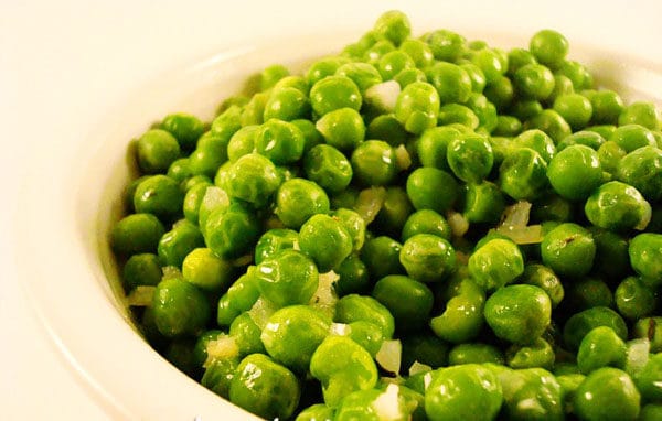 White bowl with green peas and chunks of garlic.