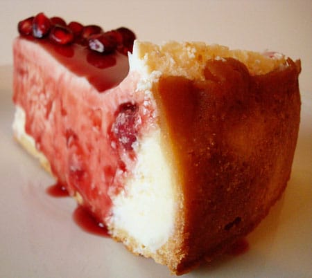 side view of a piece of cheesecake with pomegranate sauce dripping down the sides on a white plate