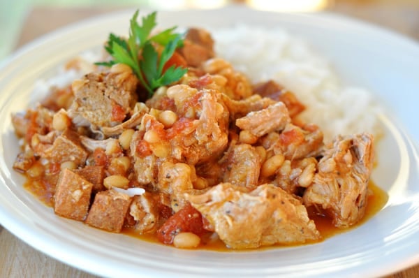 Pork and white bean stew mixture next to cooked white rice in a white bowl.