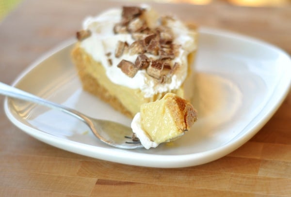 Slice of pudding pie on a white plate with whipped cream and toffee bits on top.