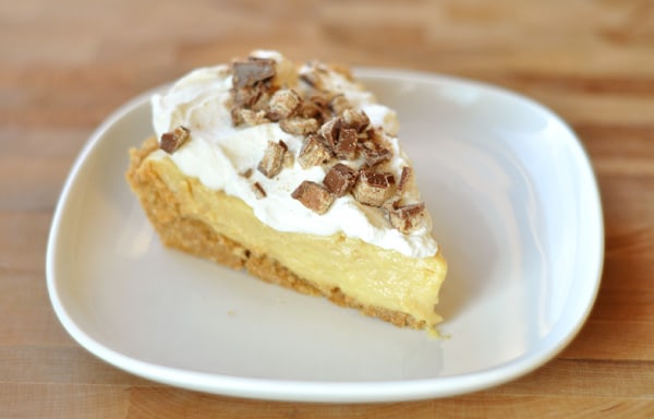 Slice of pudding pie with graham cracker crust, pudding layer, and whipped cream and toffee bits on top.