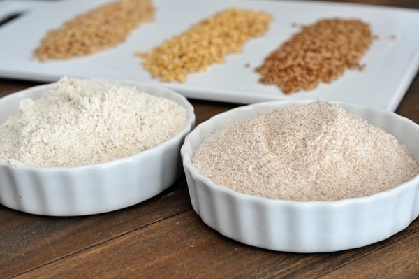 two small white bowls of ground wheat with wheat kernels on a platter behind it