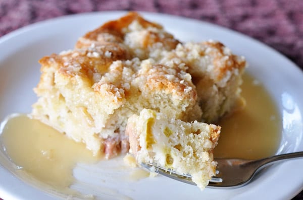 Piece of rhubarb cake with a fork taking a bite out and sauce drizzled over the top.