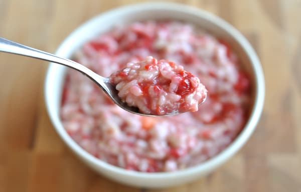 Spoon taking a bite out of a bowl of raspberry risotto oatmeal.