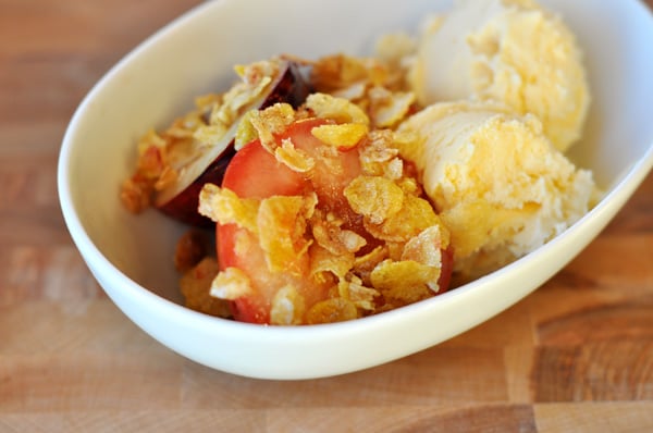 A white bowl of roasted fruit with a crunchy topping and vanilla ice cream.