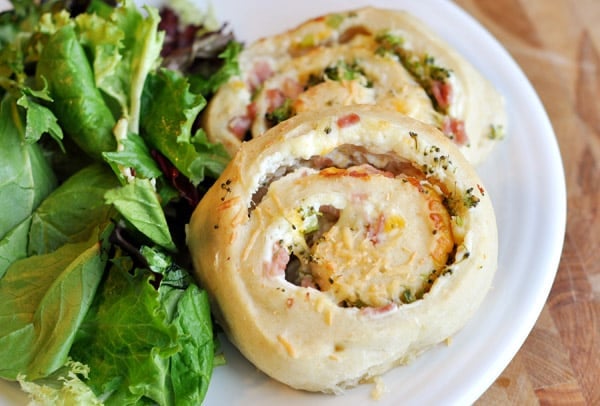 Two stuffed pinwheel rolls next to a bed of lettuce on a white plate.