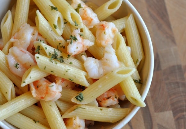 Top view of a white bowl of cooked penne and shrimp.
