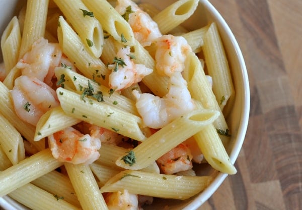 Top view of a white bowl of cooked penne and shrimp.