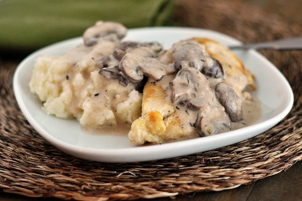 White plate with mashed potatoes and a chicken breast smothered in a mushroom sauce.