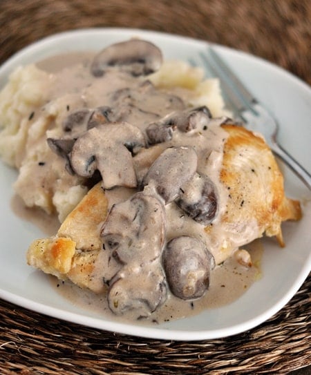 A white plate with mashed potatoes and a chicken breast covered in a mushroom sauce.