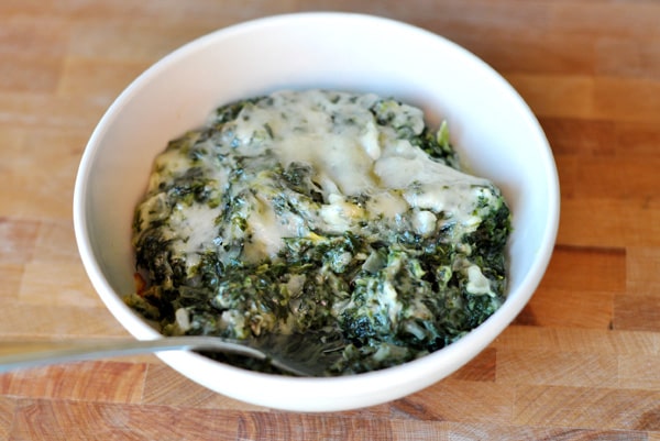 White bowl of creamy spinach with a spoon in it.