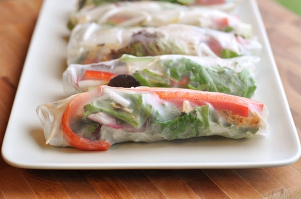 Spring rolls lined up in a row on a white platter.