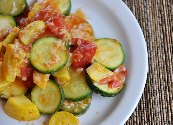 White plate of sautéed zucchini and yellow squash slices, with a tomato sauce on top.