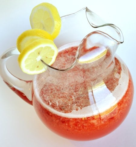 Glass pitcher with lemon slices on top and half full of strawberry lemonade.