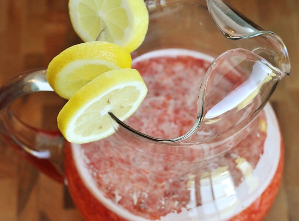 Top view of a glass pitcher full of strawberry lemonade with lemon slices on the side of the pitcher.