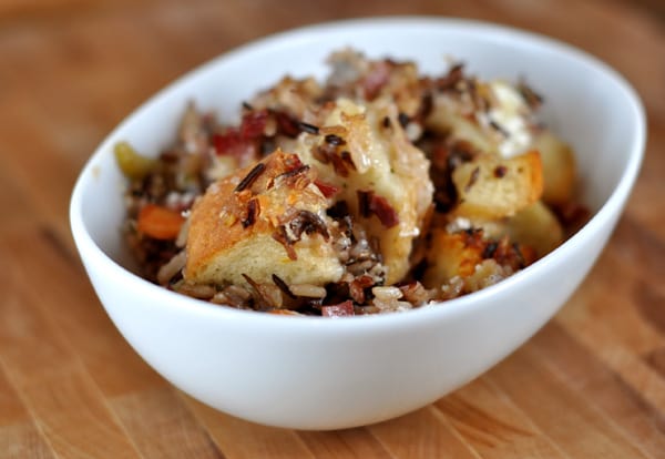 White bowl full of wild rice stuffing with big chunks of bread and goat cheese.