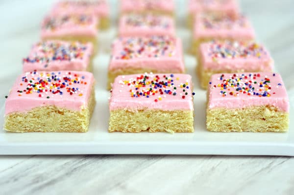 cut up frosted and sprinkled sugar cookie bars on a white platter