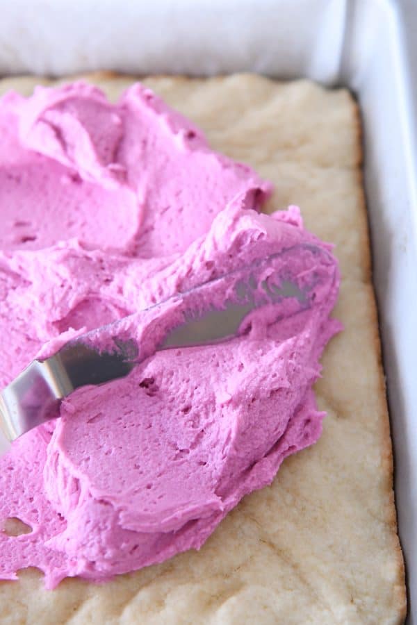 A pan of sugar cookie dough getting frosted with pink frosting.