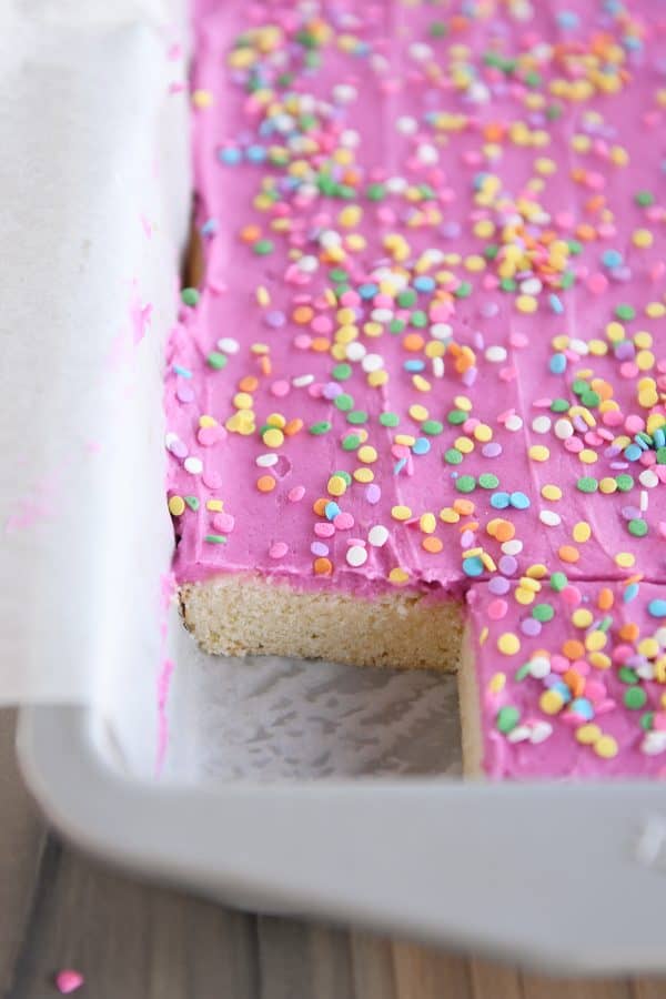 Pan of frosting-covered sugar cookie bars with one bar cut out in the corner.