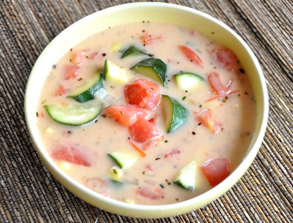 Top view of a bowl of soup with chunks of zucchini and tomatoes.