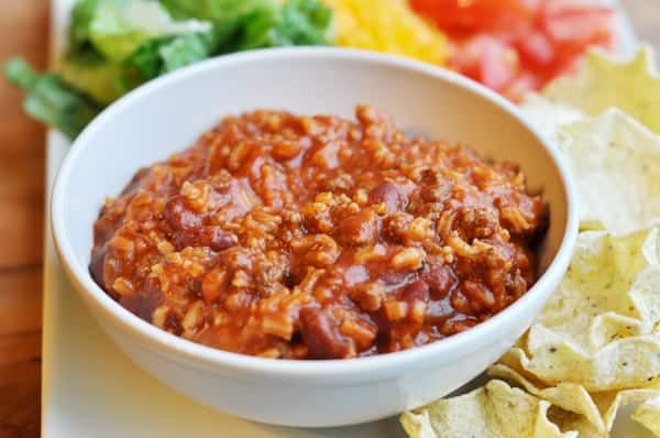 White bowl of taco salad beef mixture with all the toppings around the side.