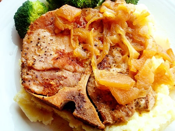 Bone-in pork chop with cooked onions on top.