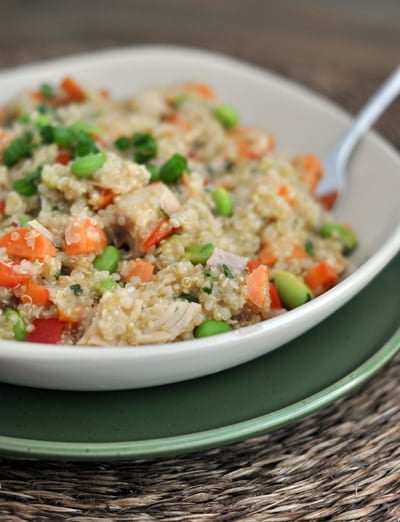 White bowl with cooked quinoa salad filled with chicken, edamame, and peppers.