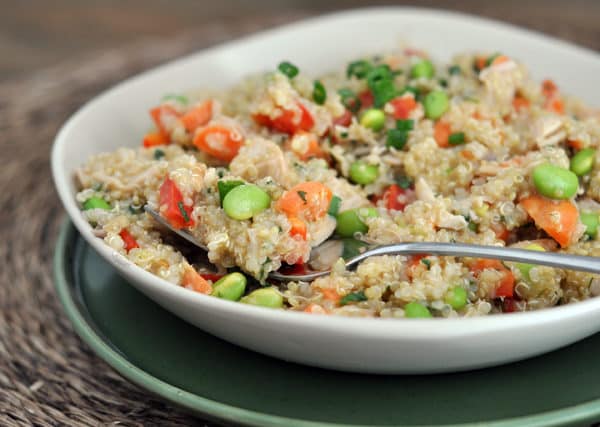 White bowl of cooked quinoa salad with edamame, peppers, and green onions.