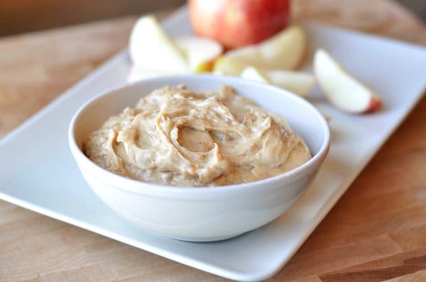 White bowl full of dip with apple slices next to it on a white rectangular plate.