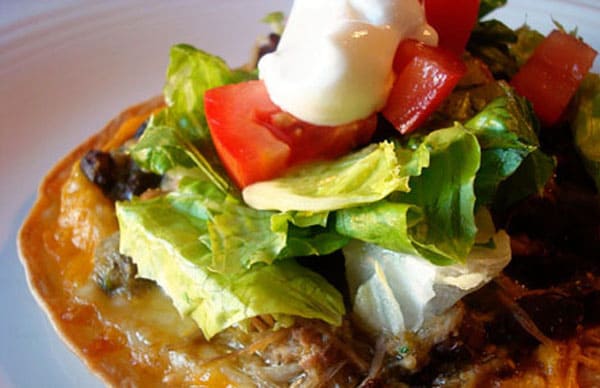 Tostada with lettuce, tomato, sour cream, and avocado.