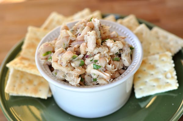 White ramekin of white bean tuna salad on a green plate with crackers surrounding the salad.