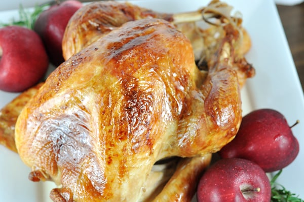Top view of a roasted whole turkey with four red apples on the side on a white platter.