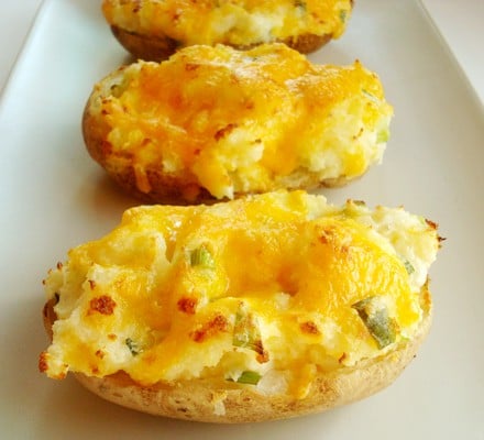 Baked potatoes cut in half with melted cheese and chopped chives on a white plate.