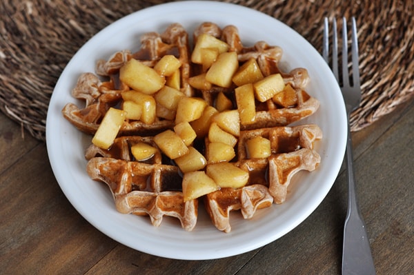 top view of a waffle on a white plate covered in cooked apples and cinnamon