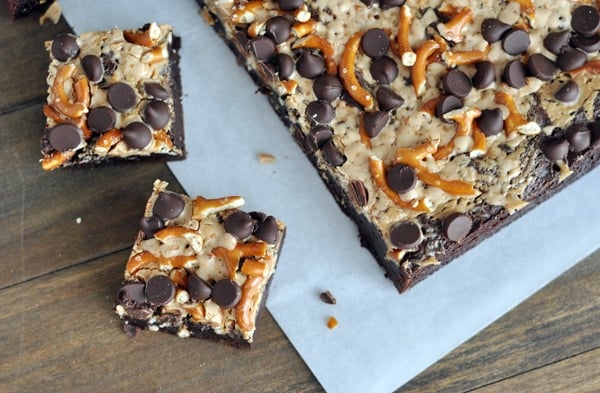 Top view of a slap of pretzel and chocolate chip topped brownies with two brownies cut off the slab on the side.