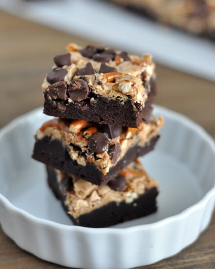 Three pretzel and chocolate chip topped brownies stacked on top of each other in a white ramekin.