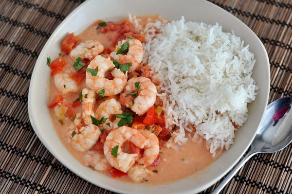 Top view of cooked shrimp bathed in a tomato sauce mixture with cooked white rice on the side.