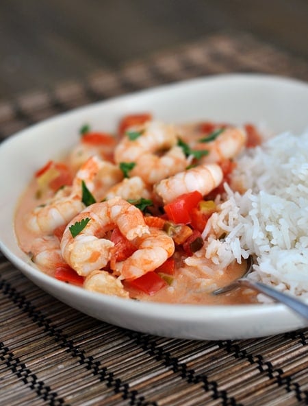 A white bowl with cooked shrimp in a garlic lime tomato sauce and cooked white rice.