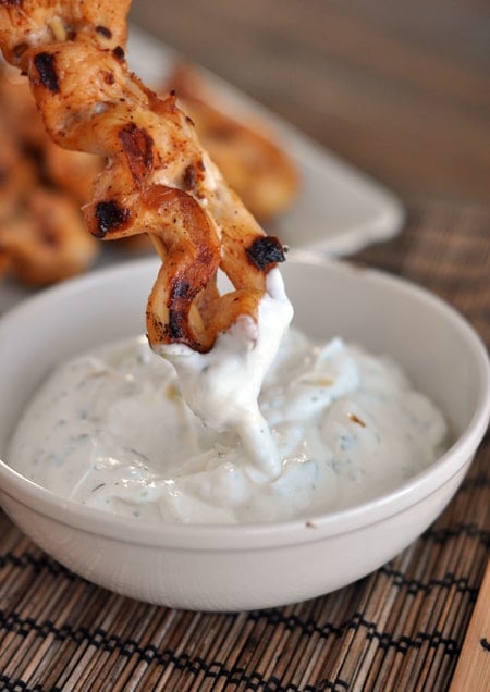 A grilled chicken skewer being dipped in a creamy sauce.